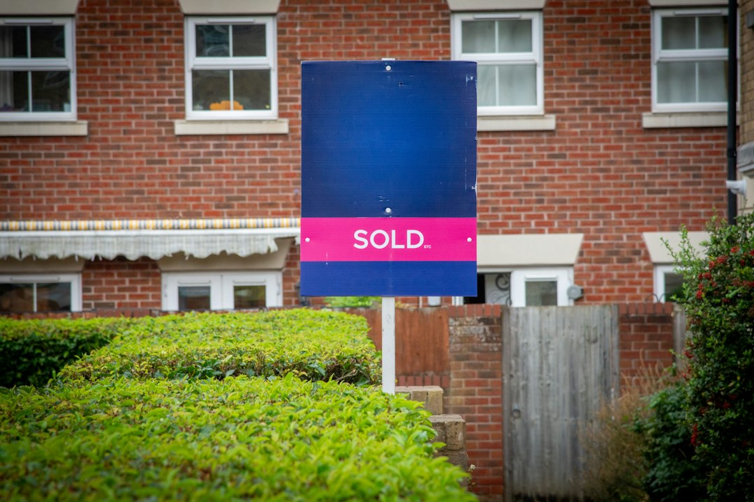A smiling couple stands proudly in front of their house next to a real estate sign that says 'Sold', representing a successful home sale.